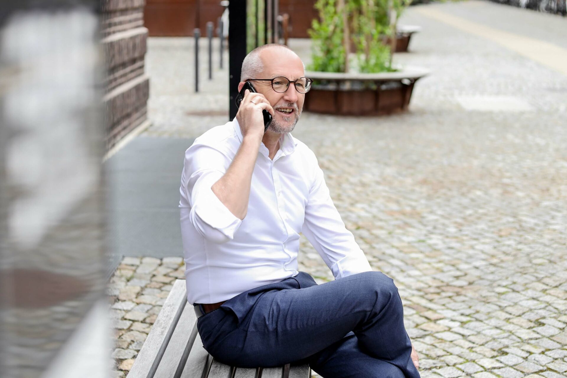 Gerd Widule, Unternehmensberater für Nachhaltigkeit, im weißen Hemd auf einer Bank sitzend mit Handy am Ohr
